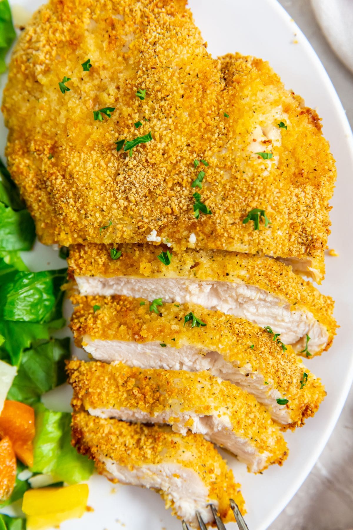 white plate with chicken cut up next to a salad