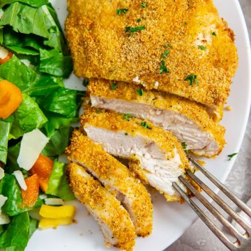 white plate with cut up chicken and salad on plate. fork on plate