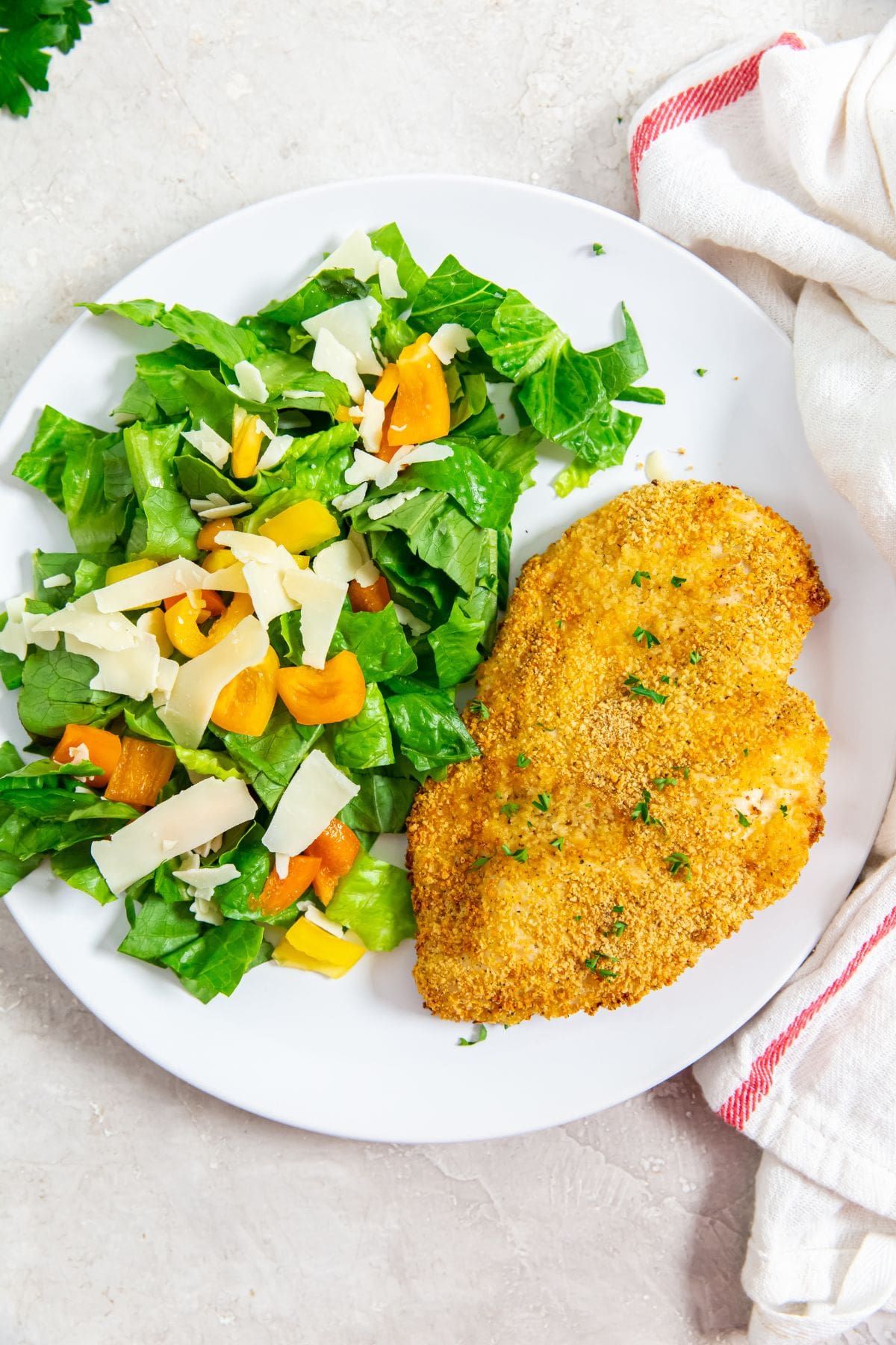 white plate with chicken and salad on plate parsley and pink towel in the back