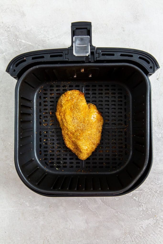 black air fryer with raw chicken breast inside