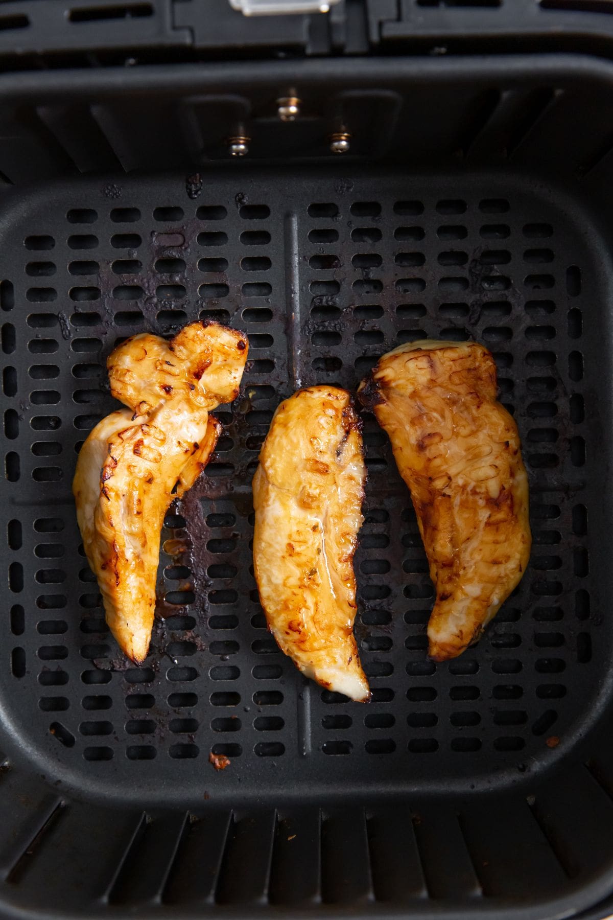 black air fryer with cooked chicken inside