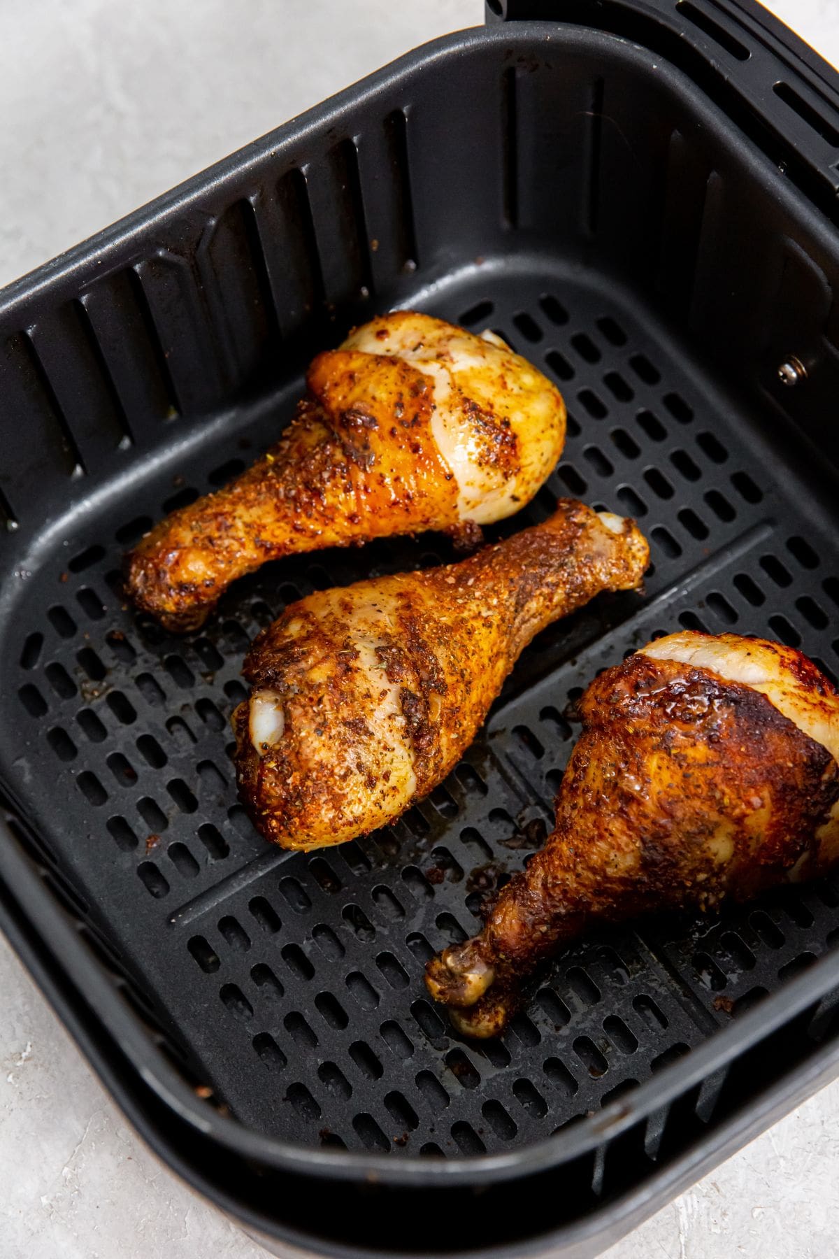 black air fryer with cooked blackened chicken legs in it