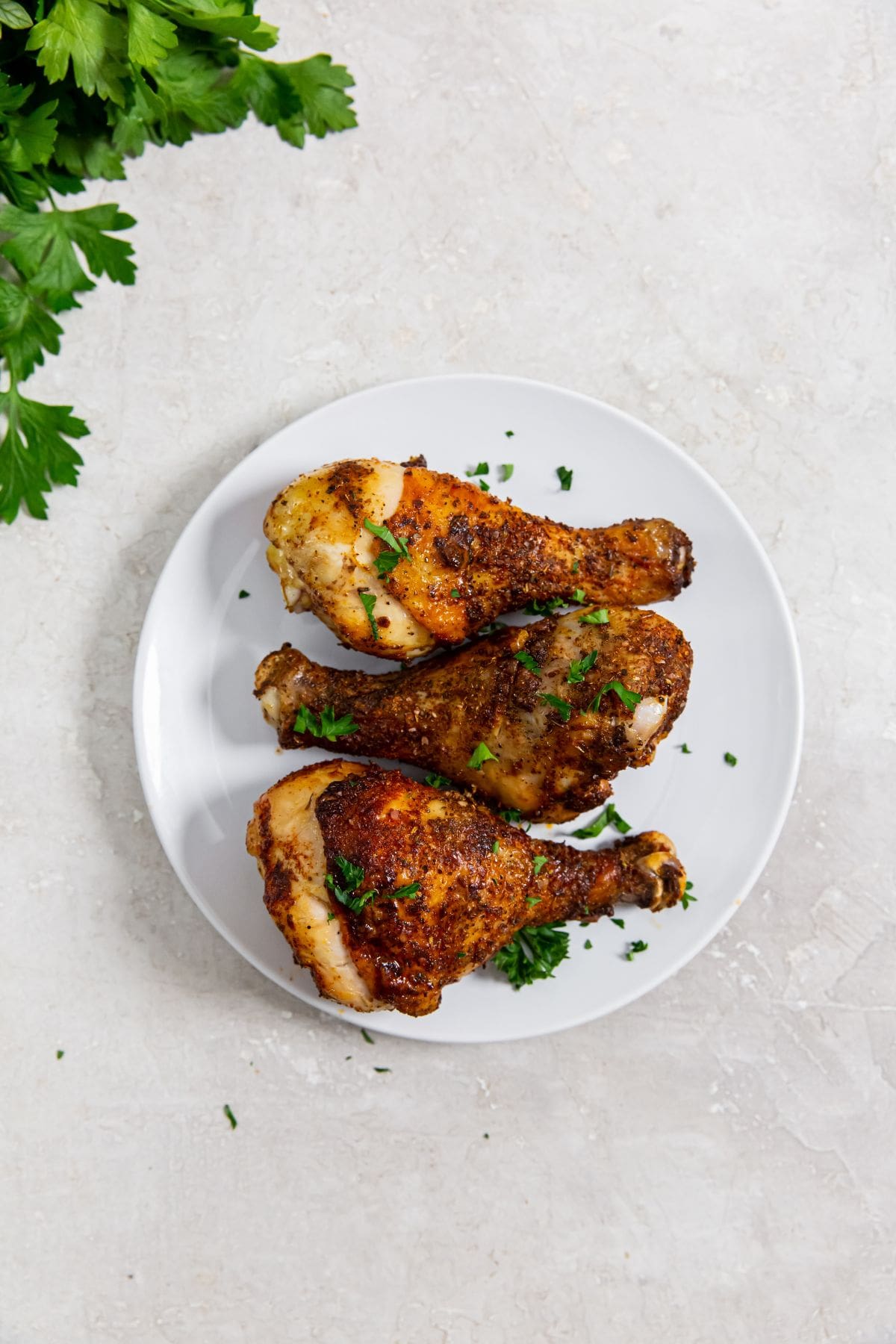 3 chicken legs on a white plate topped with parsley 