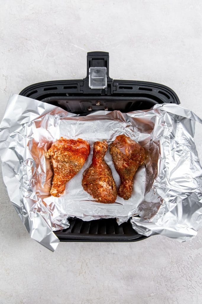 black air fryer with aluminum foil and raw chicken inside