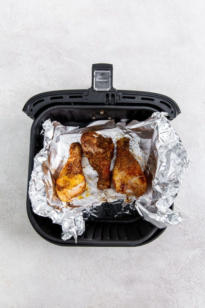 Black air fryer with aluminum foil and cooked chicken inside