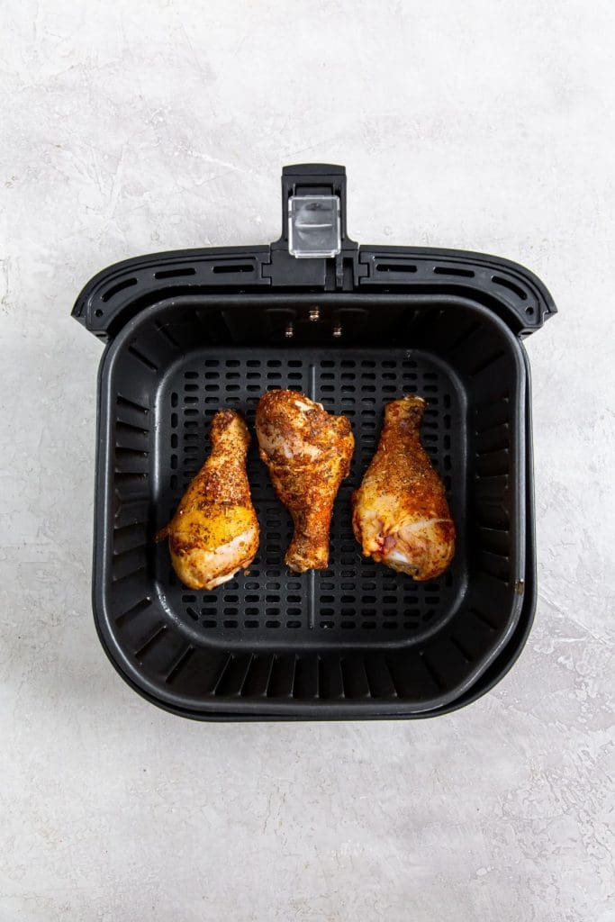 black air fryer with cooked chicken legs in it