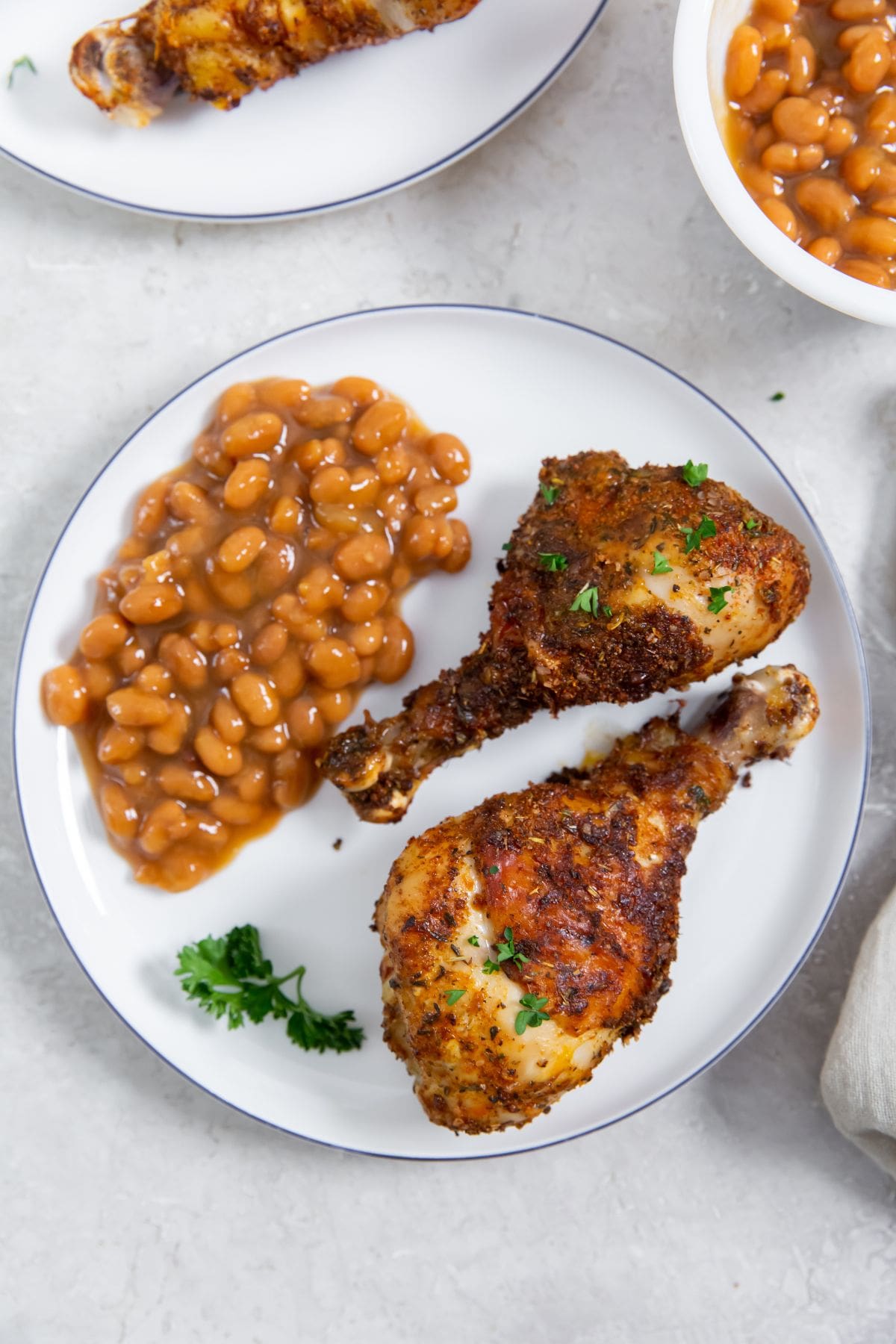 white plate with chicken legs and bake beans on it