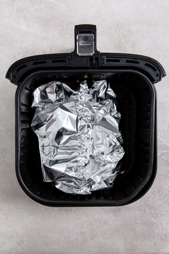 black air fryer with aluminum foil and chicken wrapped inside.