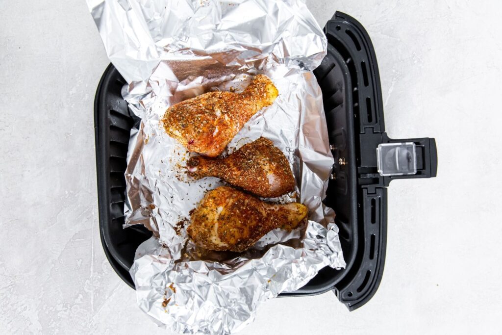 black air fryer with aluminum foil and raw chicken inside