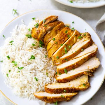 white plate with chicken thighs and rice on it parsley sprinkled on top. Naan on the side gray towel and parsley in the back