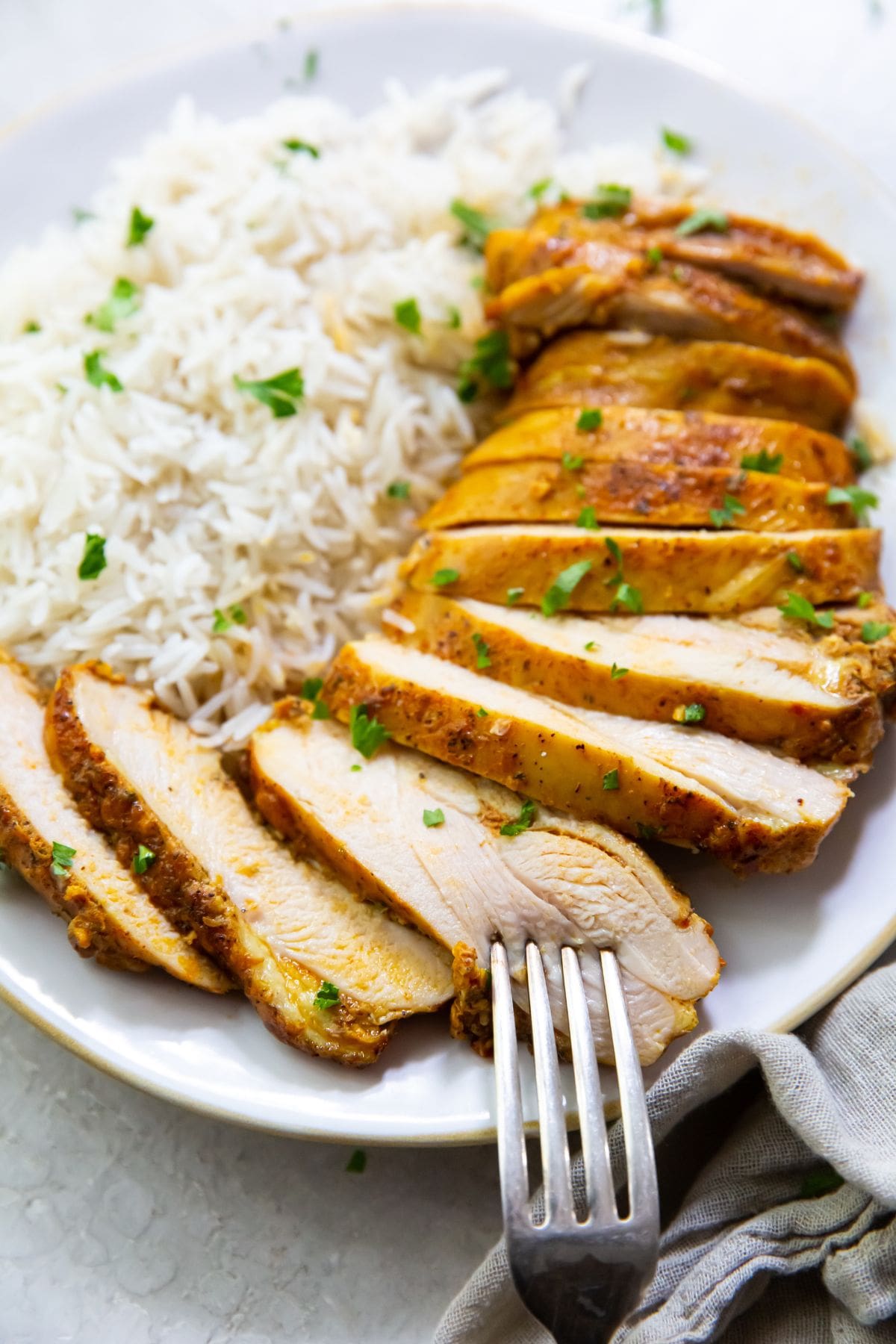 white plate with chicken thighs and rice on it parsley sprinkled on top. Naan on the side gray towel and parsley in the back  fork on the plate