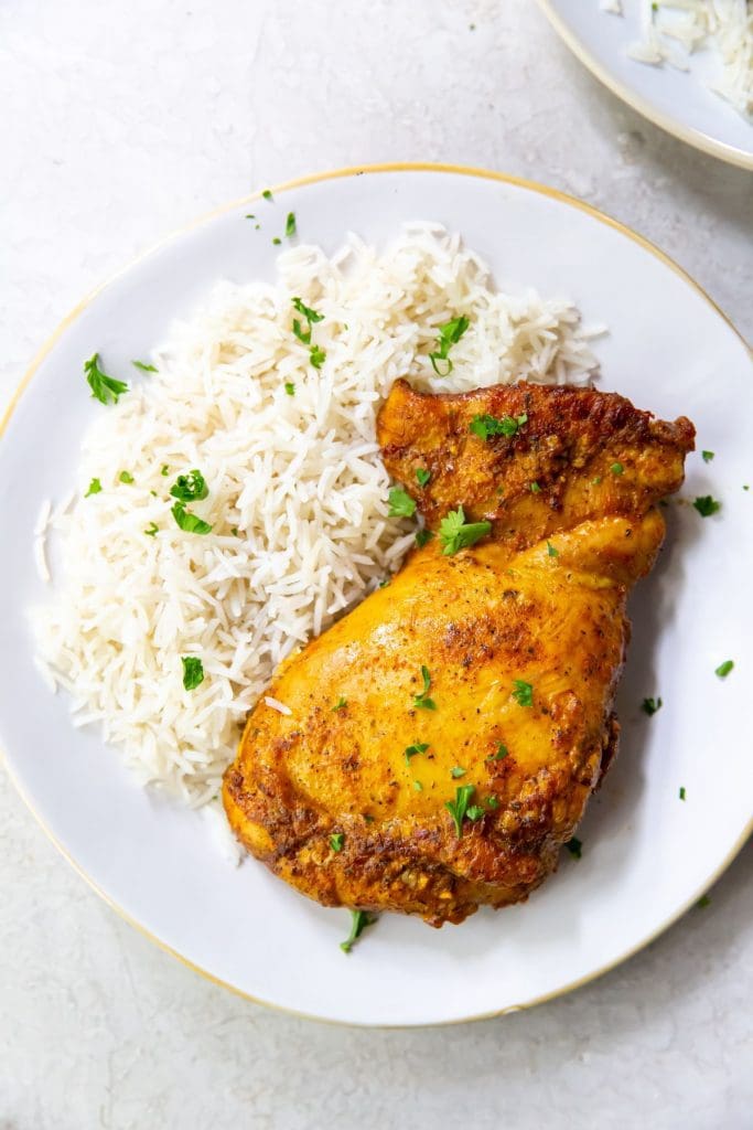 Trader Joe's shawarma chicken thighs cooked on a white plate topped with parsley and served with basmati rice