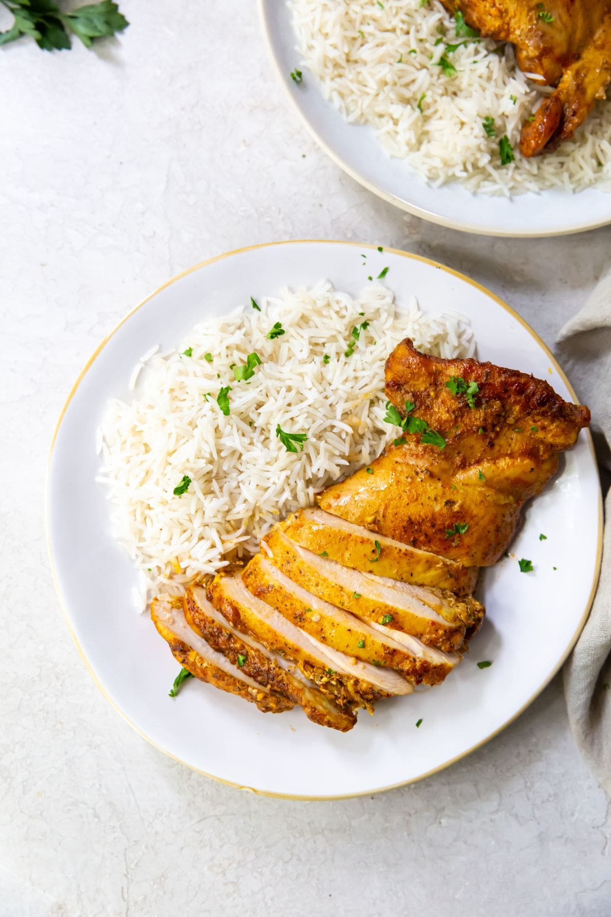 white plate with chicken thighs and rice on it parsley sprinkled on top. Naan on the side gray towel and parsley in the back