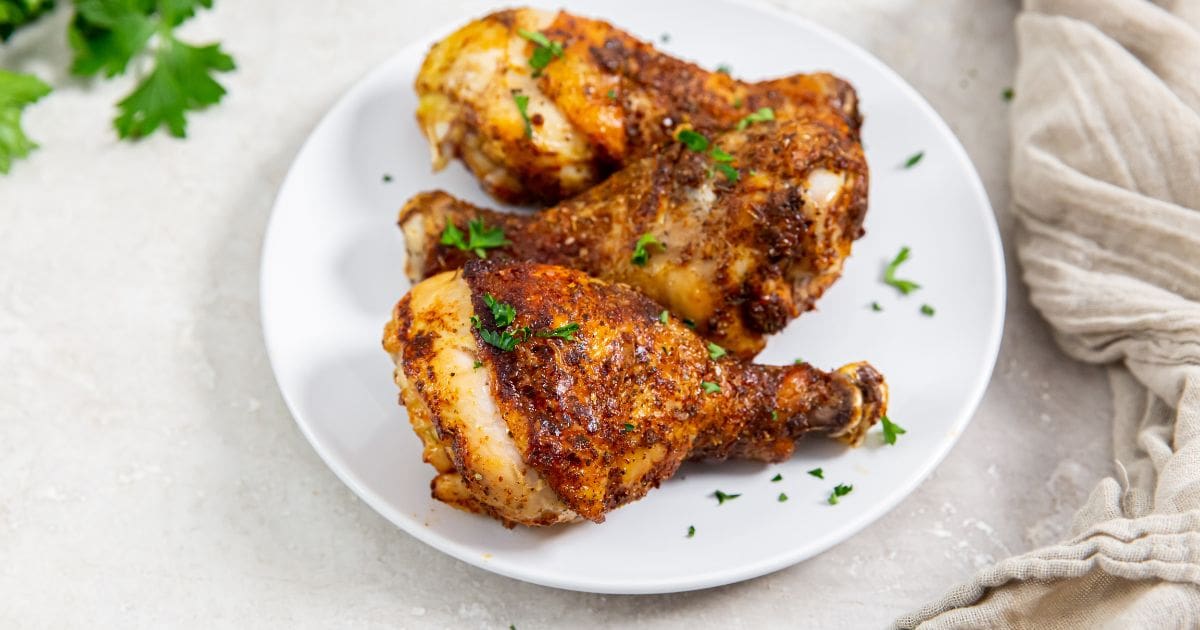 white plate with chicken legs and parsley in the back