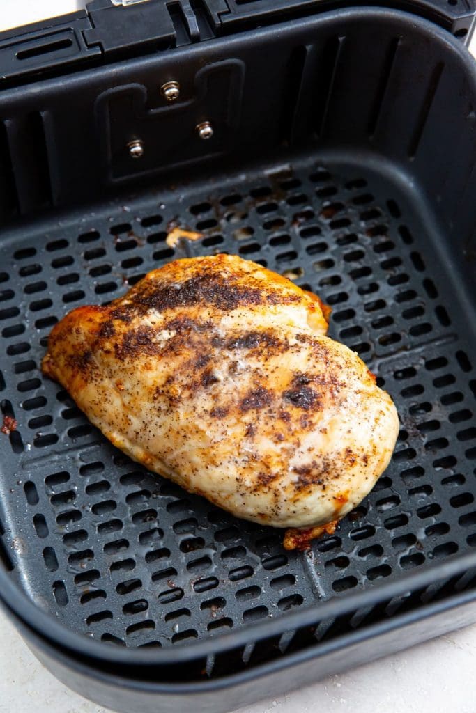 black air fryer basket with cooked chicken inside it.