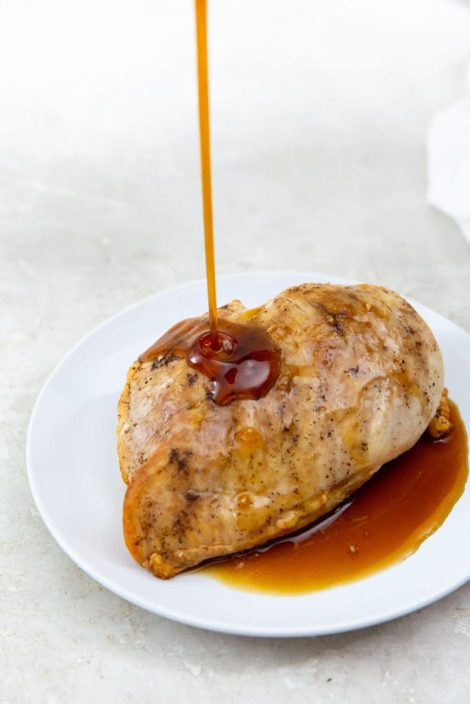 white plate with cooked chicken on it. glaze being poured on top.