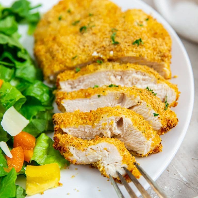 white plate with cut up chicken and salad on plate. fork on plate