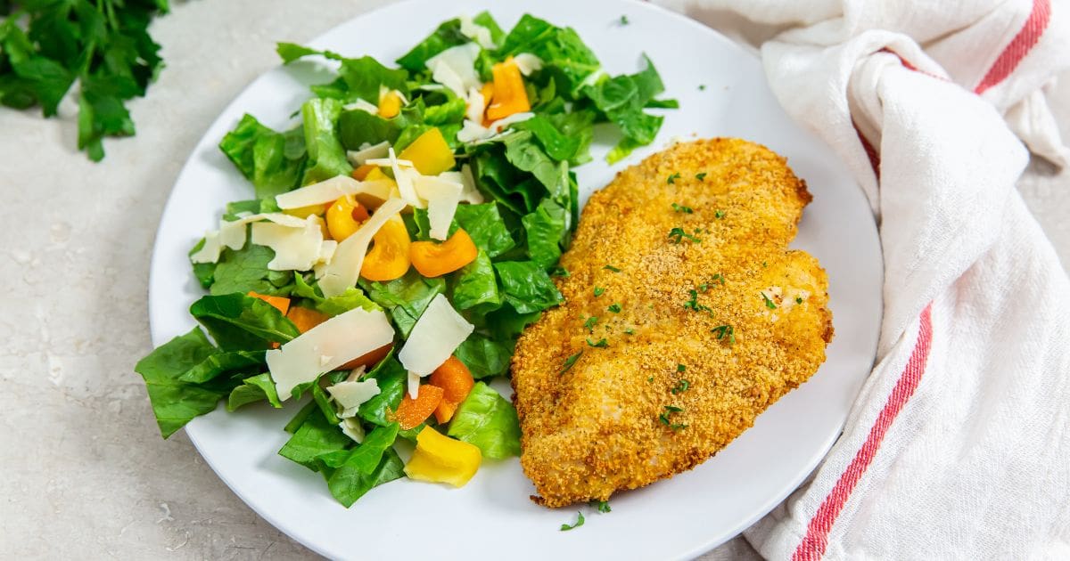 white plate with chicken and salad on plate parsley and pink towel in the back