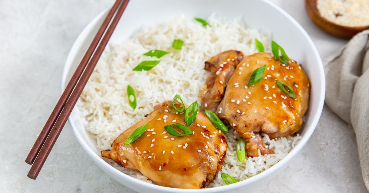 white bowls with rice and chicken thighs inside. Green onions on top. Gray towel in the back. sesame seeds and green onion in a brown bowl 