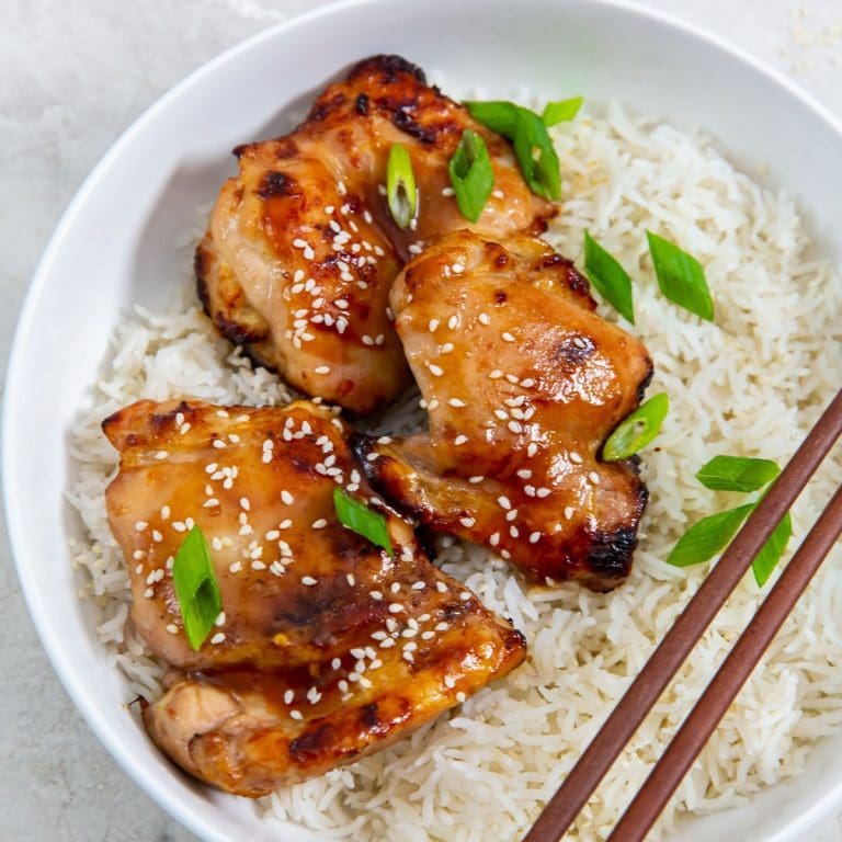 white bowl with rice and chicken inside. green onion sprinkled on top.