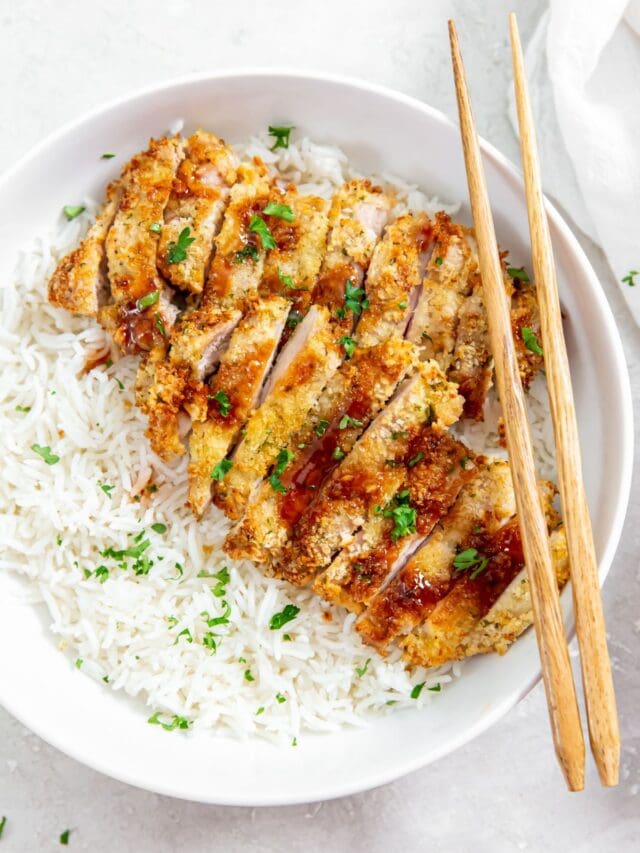 chicken and rice in a white bowl. chopsticks on the side of the bowl parsley and white towel in the back