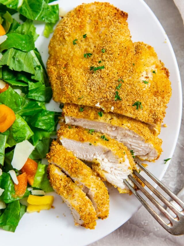 white plate with cut up chicken and salad on plate. fork on plate