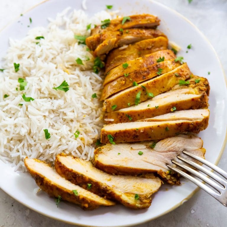 white plate with chicken thighs and rice on it parsley sprinkled on top. Naan on the side gray towel and parsley in the back