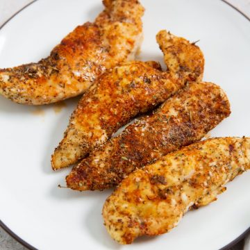 white plate with chicken tenders with parsley. parsley in the back with a towel.