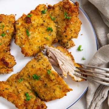 plate with chicken thighs on it. parsley and towel in the back