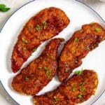 white plate with chicken on it parsley and bbq sauce in the back
