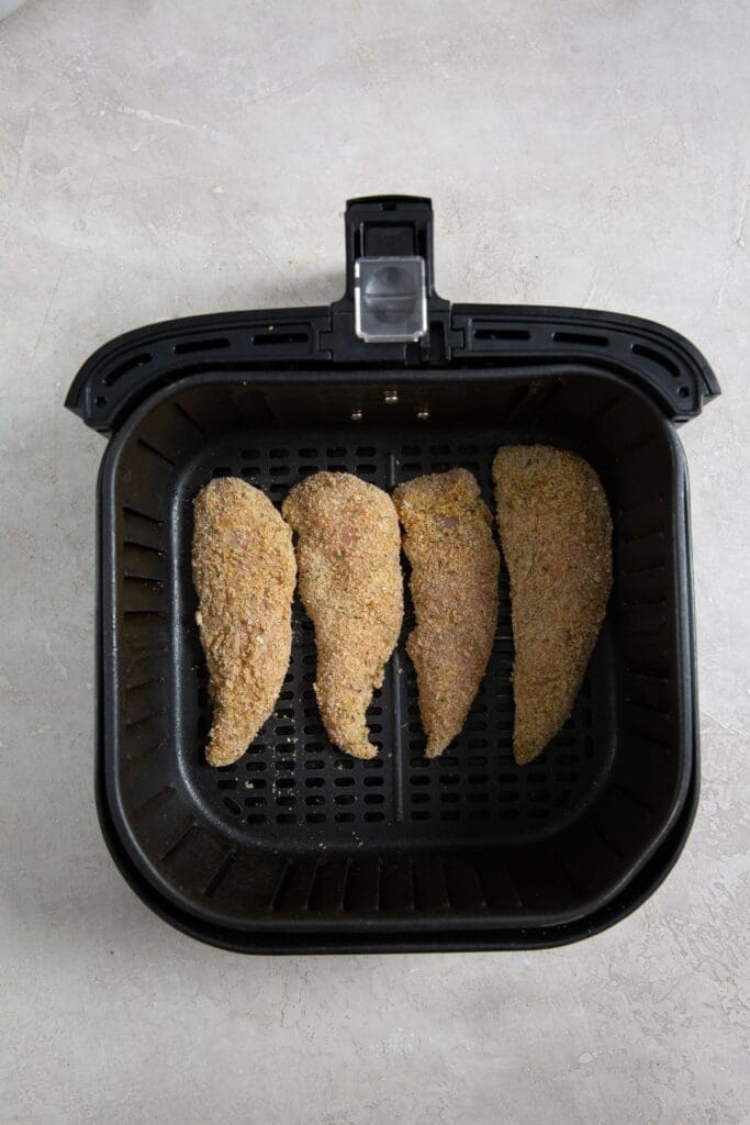 black air fryer basket with raw chicken inside