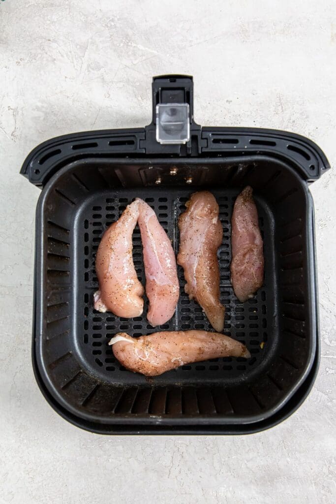 black air fryer with raw chicken inside