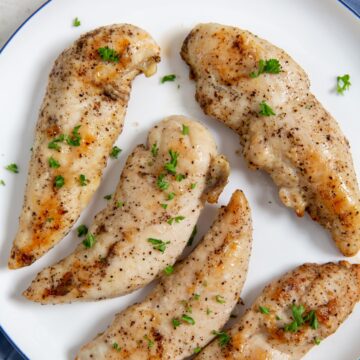 chicken on a white plate blue towel underneath parsley on top.