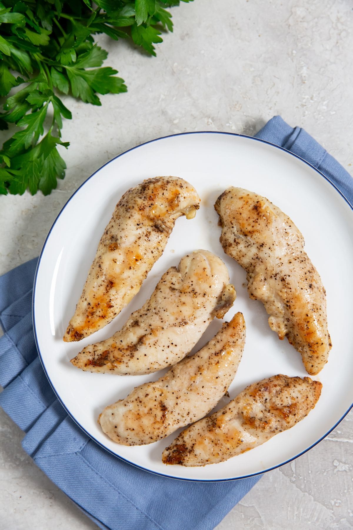 chicken on a white plate blue towel underneath . parsley on top and in the back 