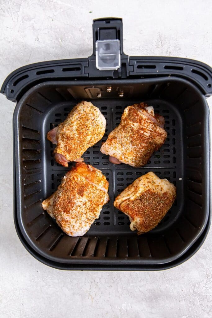 black air fryer with raw chicken inside.