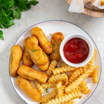 plate with chicken and fries on it parsley in the back with a bowl of fries