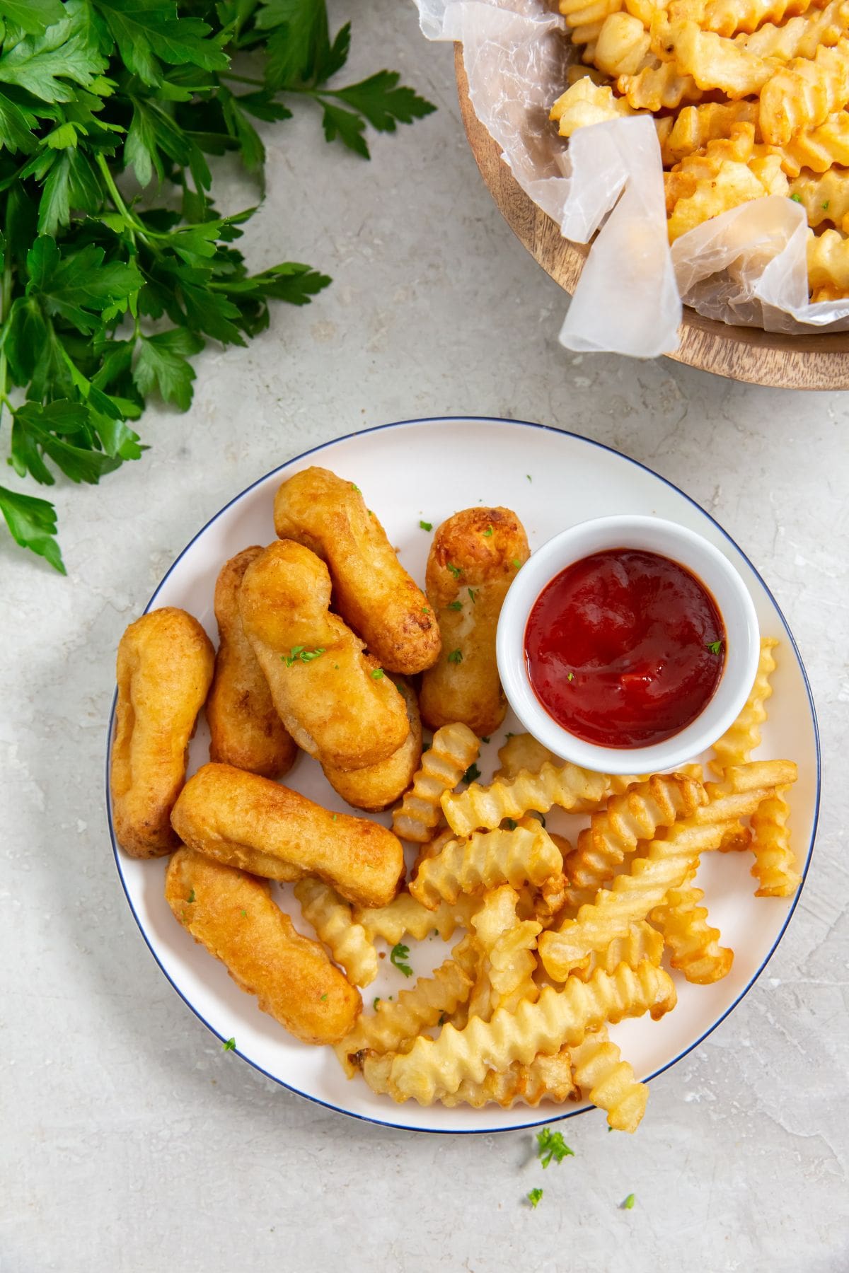 plate with chicken and fries on it parsley in the back with a bowl of fries