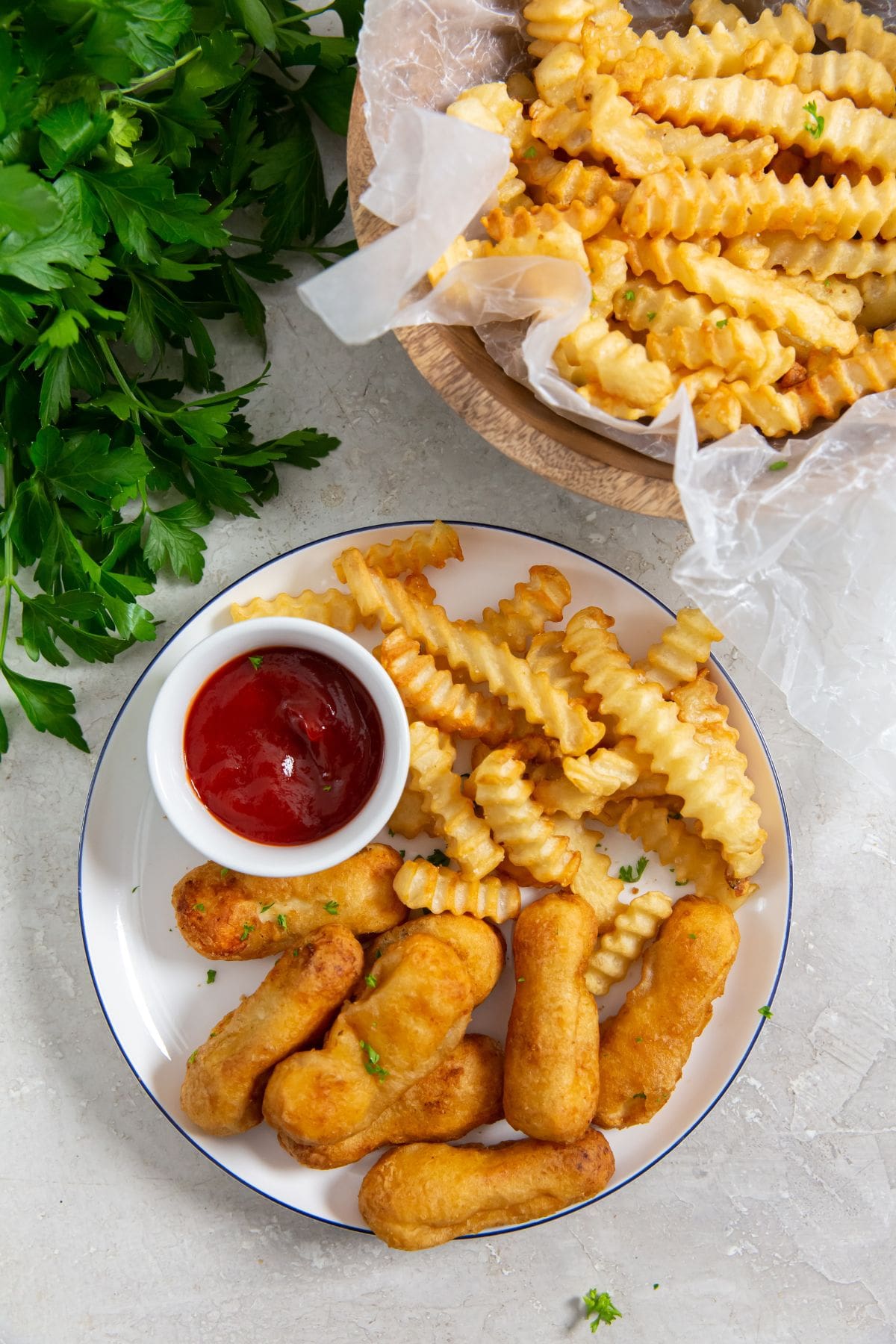 plate with chicken and fries on it parsley in the back with a bowl of fries