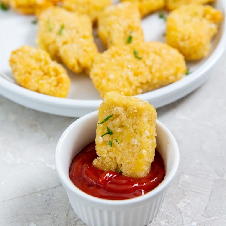 chicken dunked in a ketchup plate of nuggets next to it