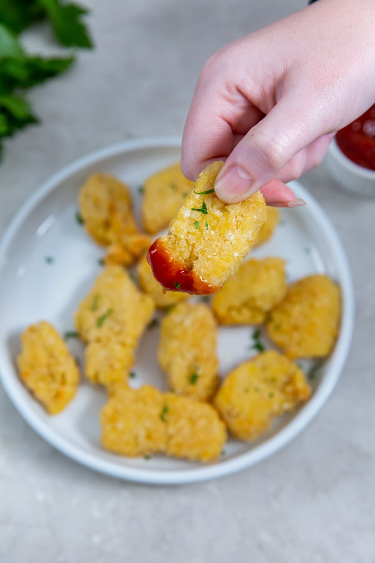 plate with nuggets one it. a person holding one nugget dunked in ketchup