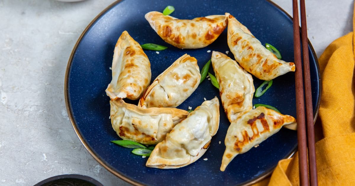 Blue plate with air fryer Trader Joe's chicken potstickers and scallions on it. chopsticks on the side of the plate. orange towel next to it.