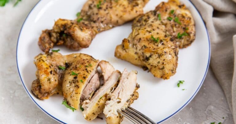 white plate with chicken on it. parsley and gray towel in the back. fork on the plate