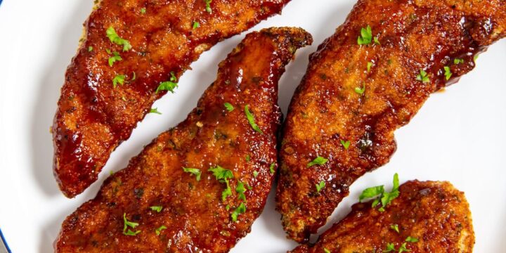 white plate with chicken on it parsley and bbq sauce in the back