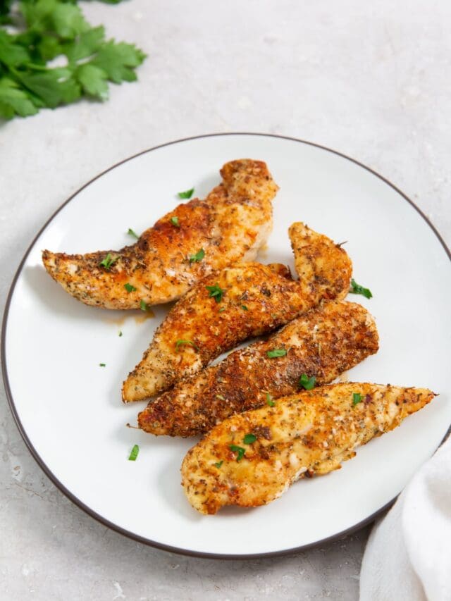 white plate with chicken tenders with parsley. parsley in the back with a towel.