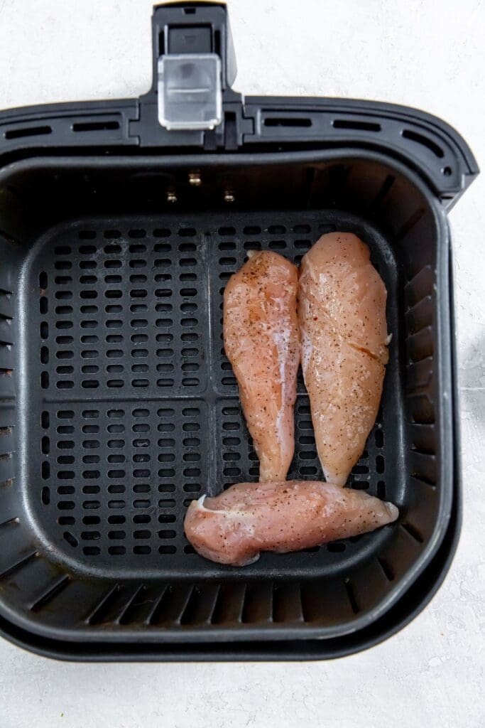 black air fryer with raw chicken inside