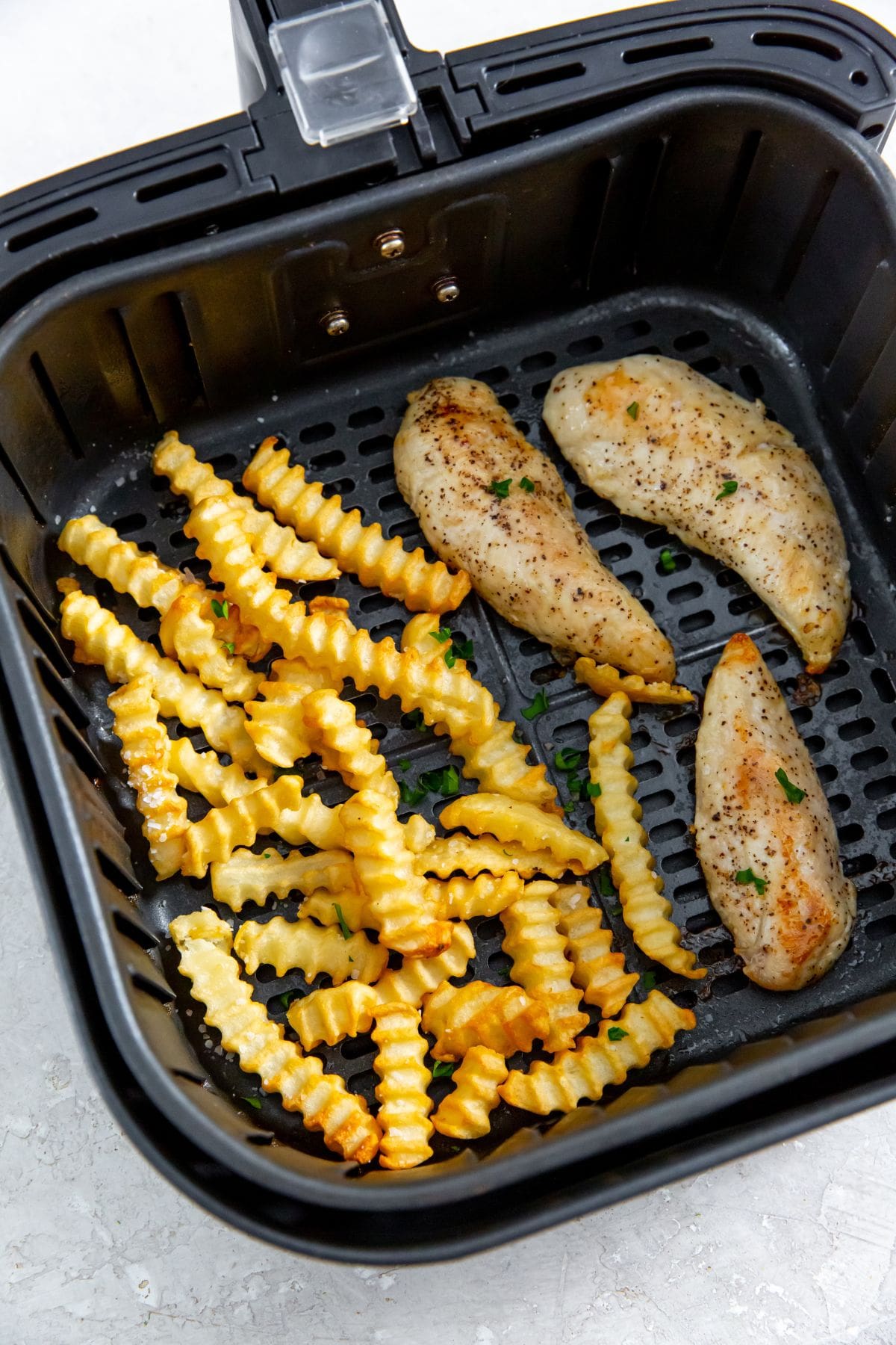 black air fryer with cooked chicken and fries inside