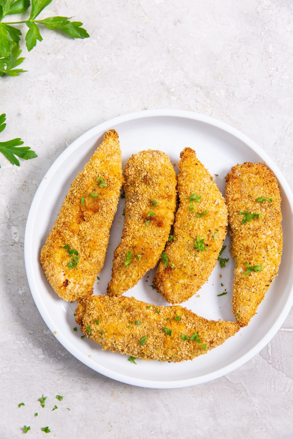 plate with chicken tenders. parsley sprinkled on top and in the back 