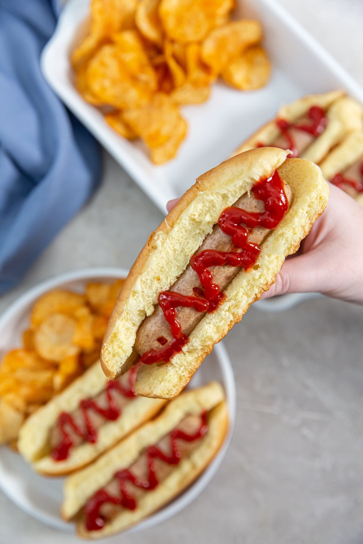 a person holding chicken sausage over top with more chicken and chips