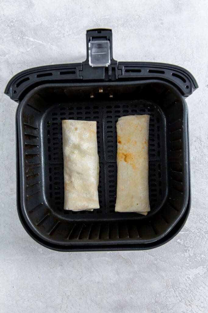 black air fryer with raw burritos inside