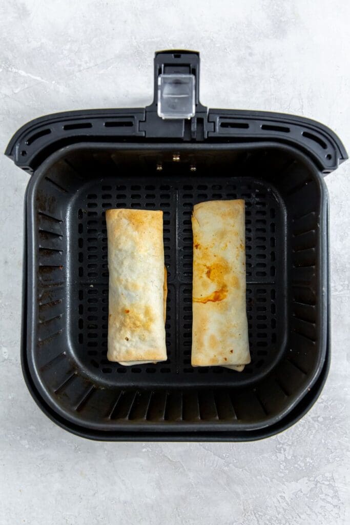 black air fryer with cooked burritos inside